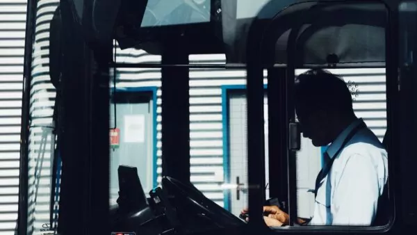 A train driver sits in the driver's compartment of a train, with his face mostly in shadow.